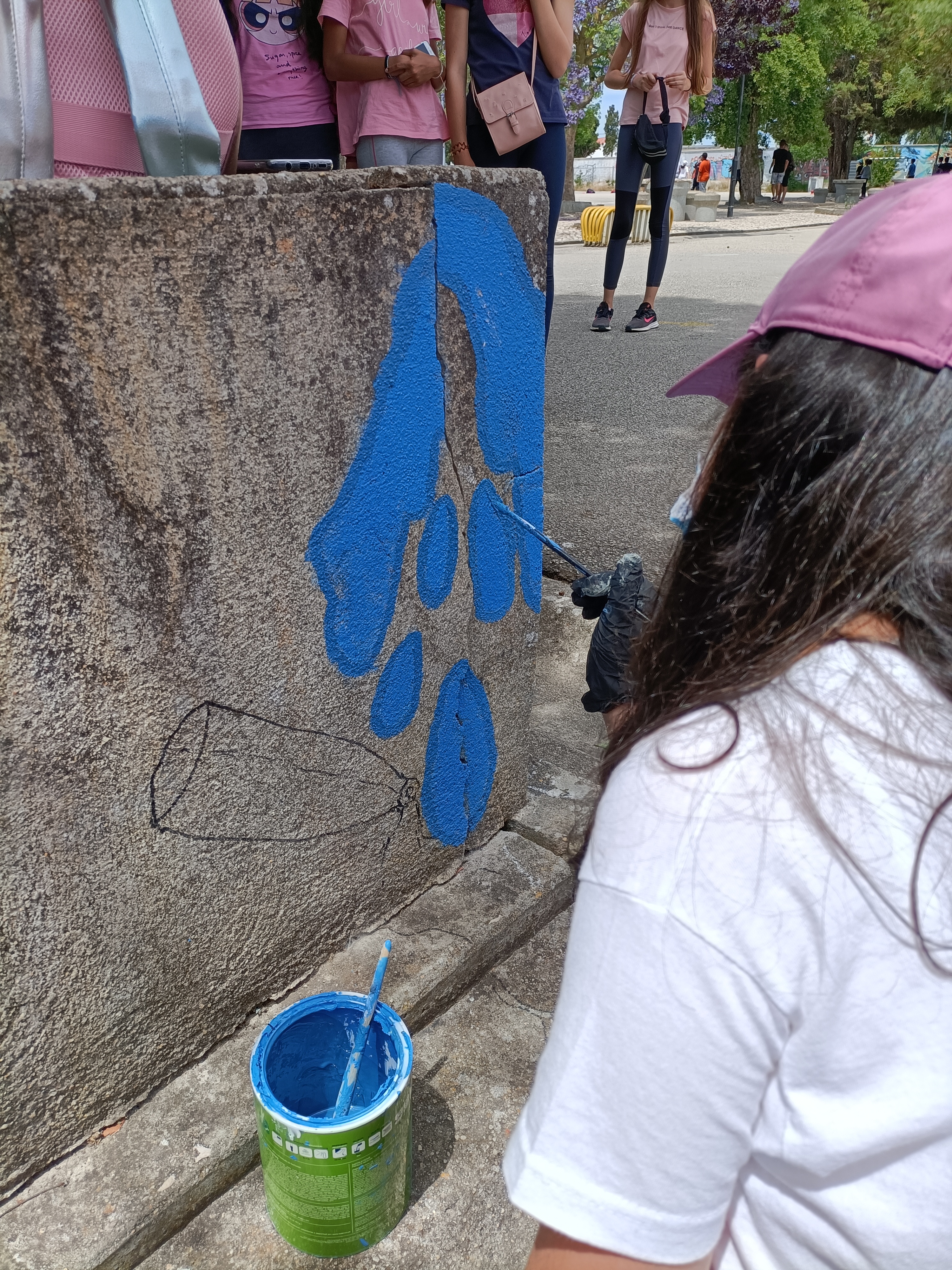 Continuação do trabalho. Uma aluna pinta as gotas de água a saírem de uma fenda (real) existente no muro .